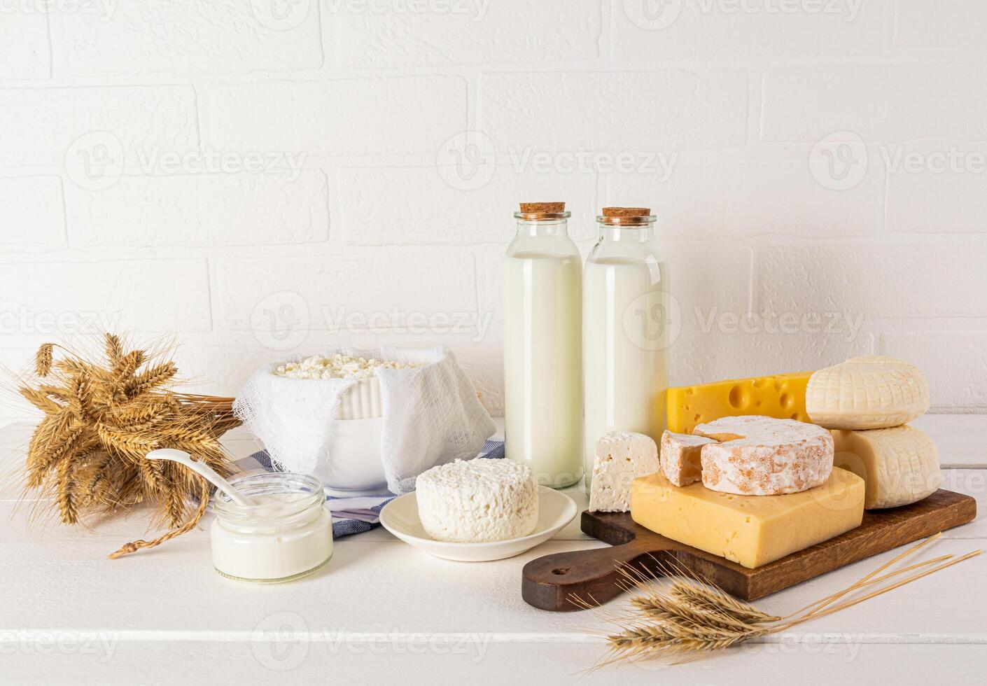 Lots of different fresh dairy products on a white wooden table and a bouquet of ears of corn. The concept of the holiday of Shavuot photo