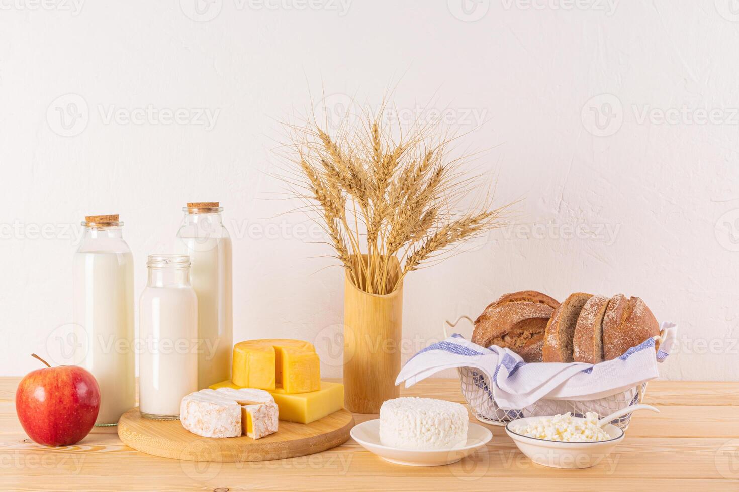 un variedad de Fresco lechería productos, pan, orejas de maíz, manzanas en un de madera mesa. trata y símbolos de el judío fiesta de shavuot. foto