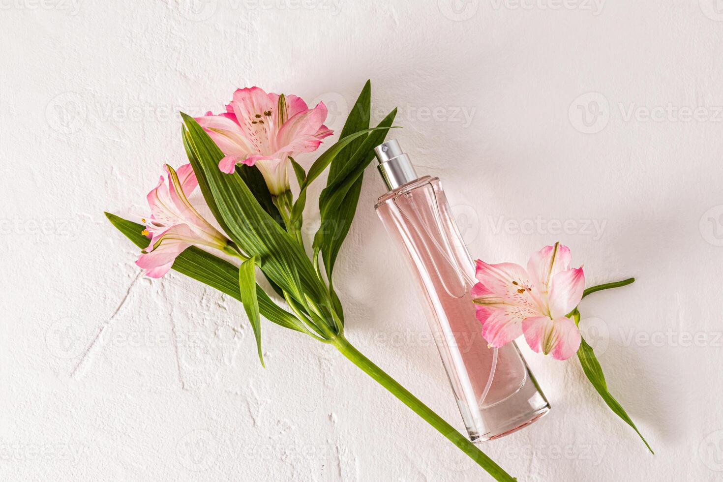 A chic bottle of women's perfume lies on a white background with delicate astromeria flowers. Top view. Empty bottle. photo