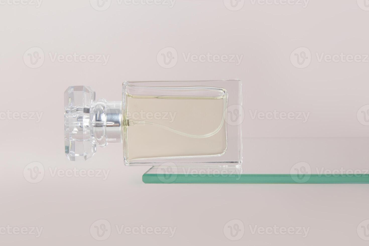 A crystal bottle of women's perfume lies on a flogging glass shelf. An empty presentation bottle. Advertising mockup of a bottle. Pastel background photo