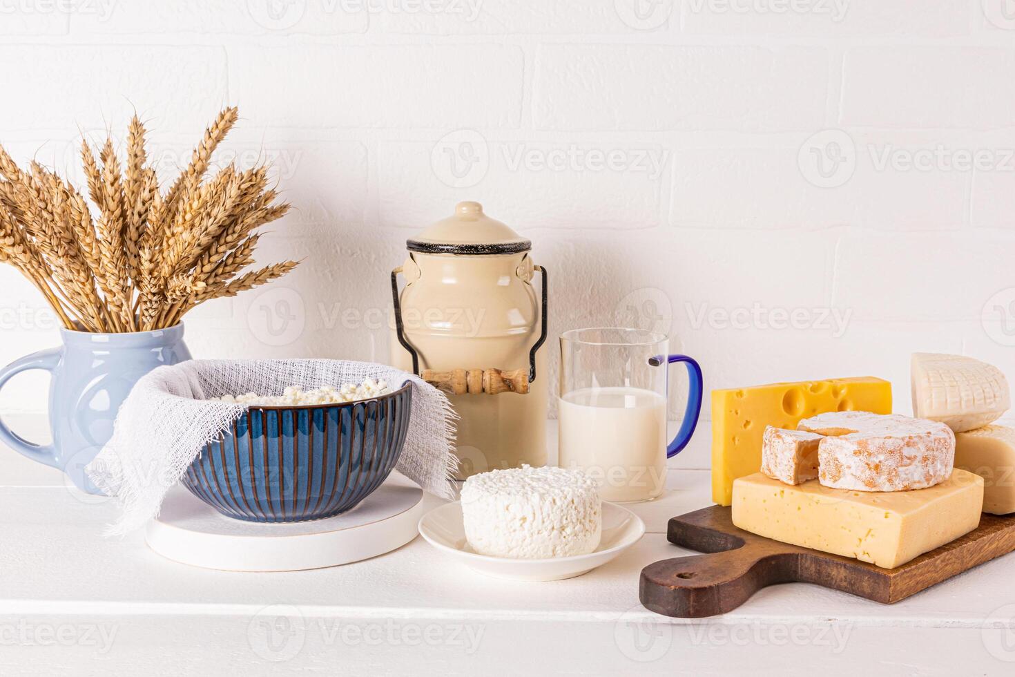 A can with milk, a bowl with fresh cottage cheese and cheese on a wooden board and a white background. Traditional dairy products for Shavuot. photo