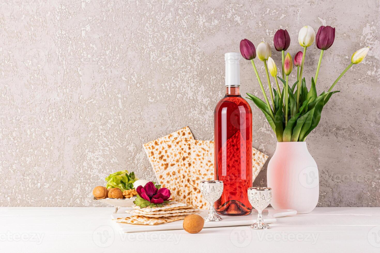 Still life for the Jewish Passover holiday. A bottle of kosher wine, freshly baked matzoth, walnuts, a vase of tulips on a light table. A copy space. photo