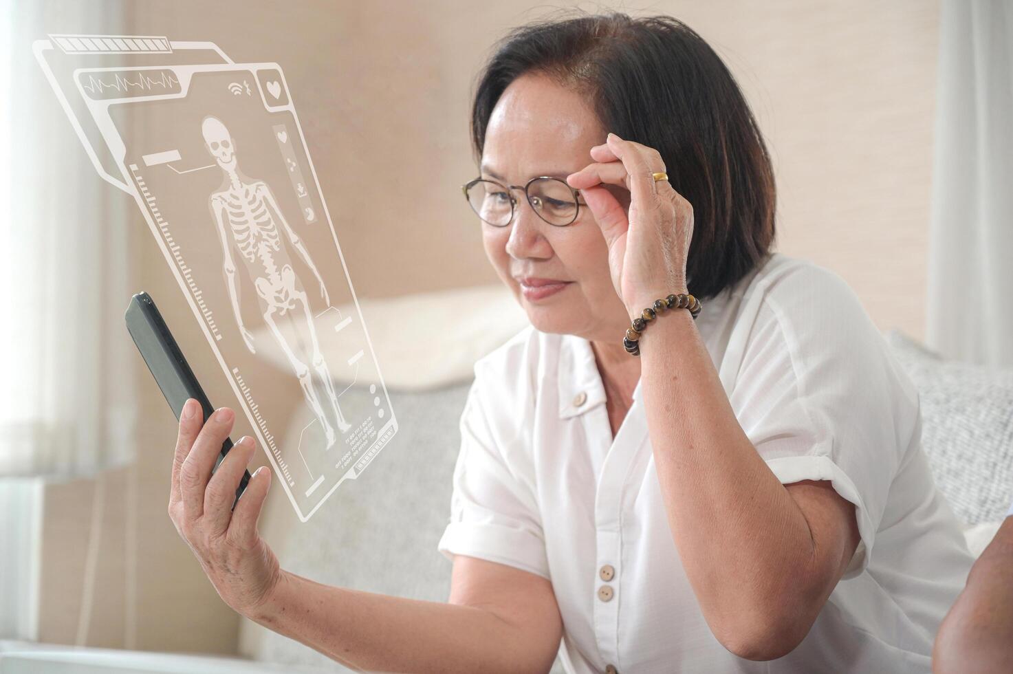 Elderly asian woman sitting on sofa is calling a video call on smartphone. The other hand grabs the glasses. photo