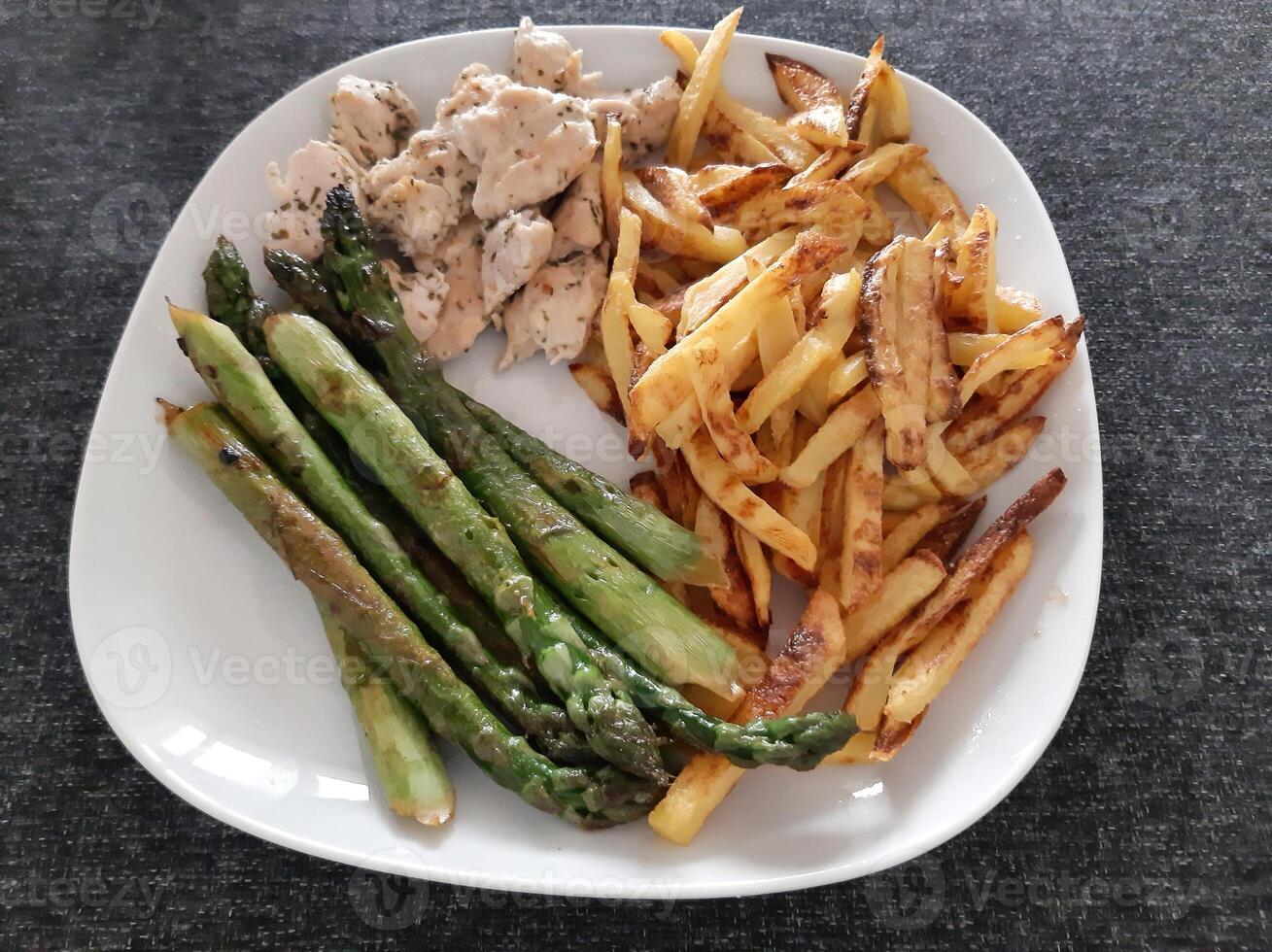 hecho en casa A la parrilla pollo con francés papas fritas y A la parrilla espárragos, servido en un blanco plato foto