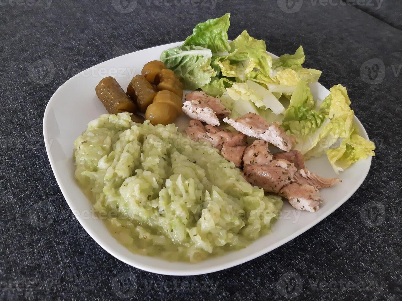 Homemade grilled chicken with zucchini stew, green salad and cucumber pickles served on a white plate photo