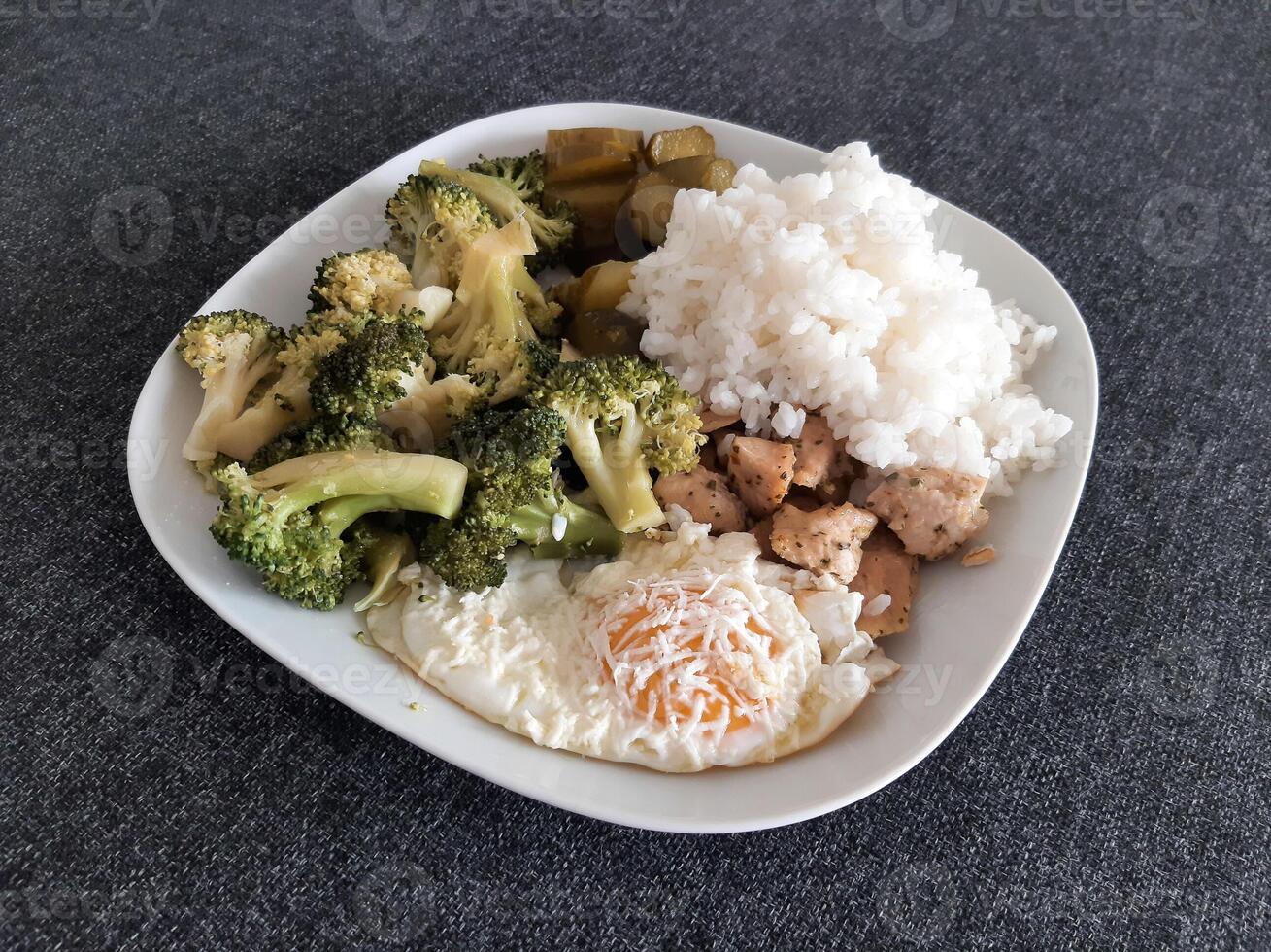 Homemade dish with broccoli, fried eggs with chese, chicken baked meat, rice and pickles served on white plate photo