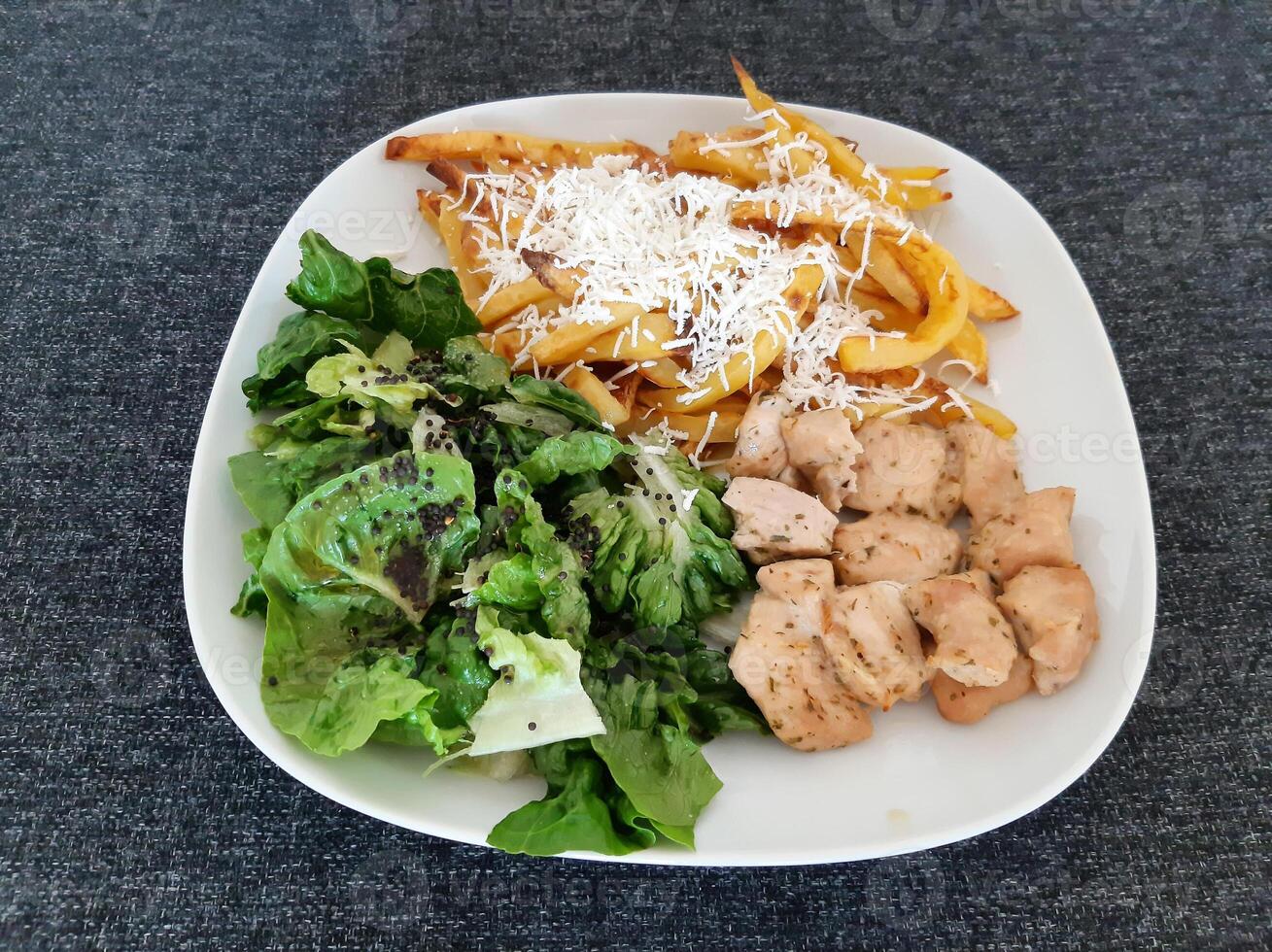 Homemade grilled chicken with french fries, cheese and green salad, served on a white plate photo