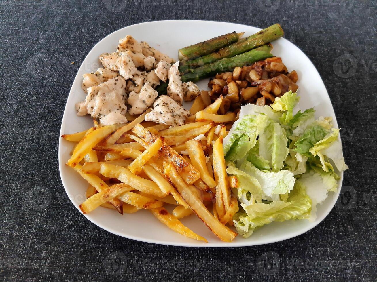 Homemade grilled chicken with french fries, asparagus, grilled chopped eggplant and green salad, served on a white plate photo