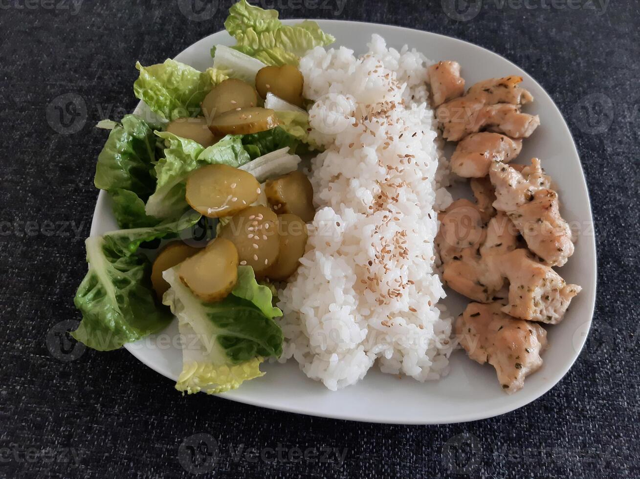 Homemade grilled chicken with green salad, rice pilaf and cucumber pickles served on a white plate photo