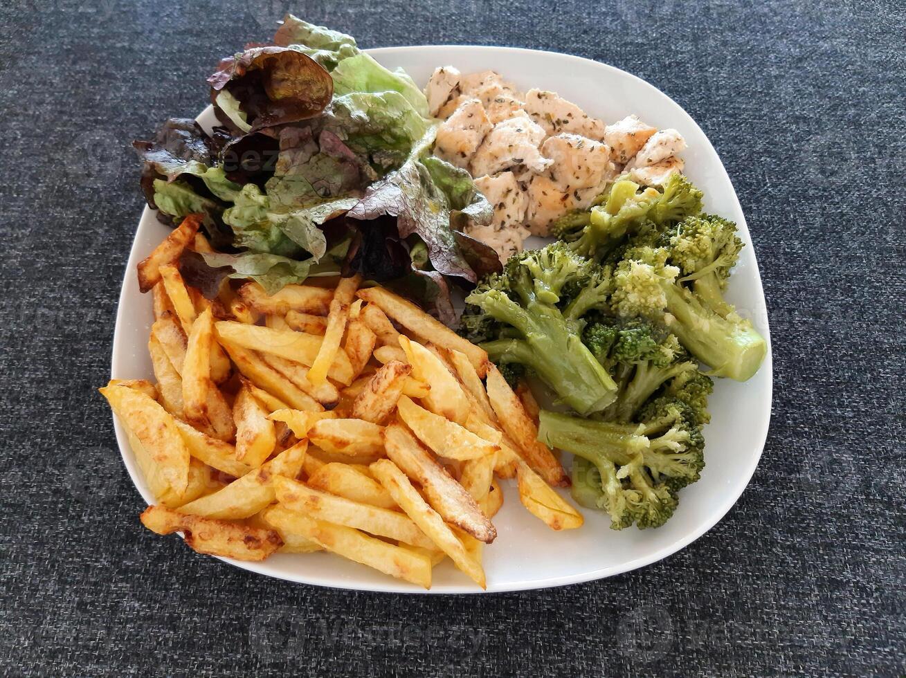 Homemade grilled chicken with french fries, broccoli and green salad, served on a white plate photo