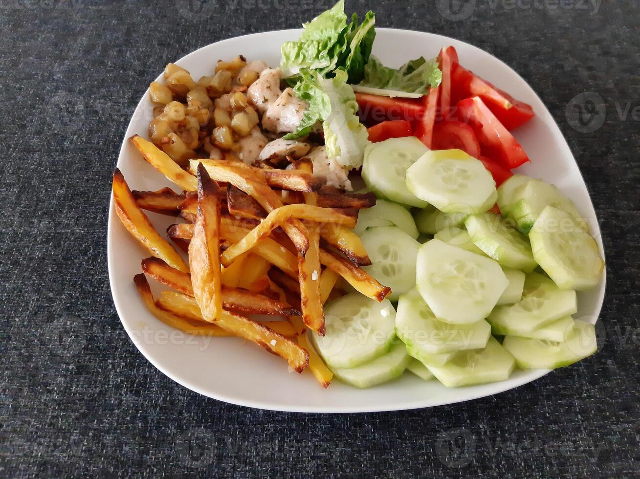 hecho en casa A la parrilla pollo con francés papas fritas, pepino, rebanado tomate y verde ensalada, servido en un blanco plato foto