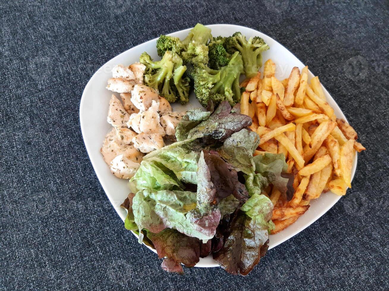 Homemade grilled chicken with french fries, broccoli and green salad, served on a white plate photo