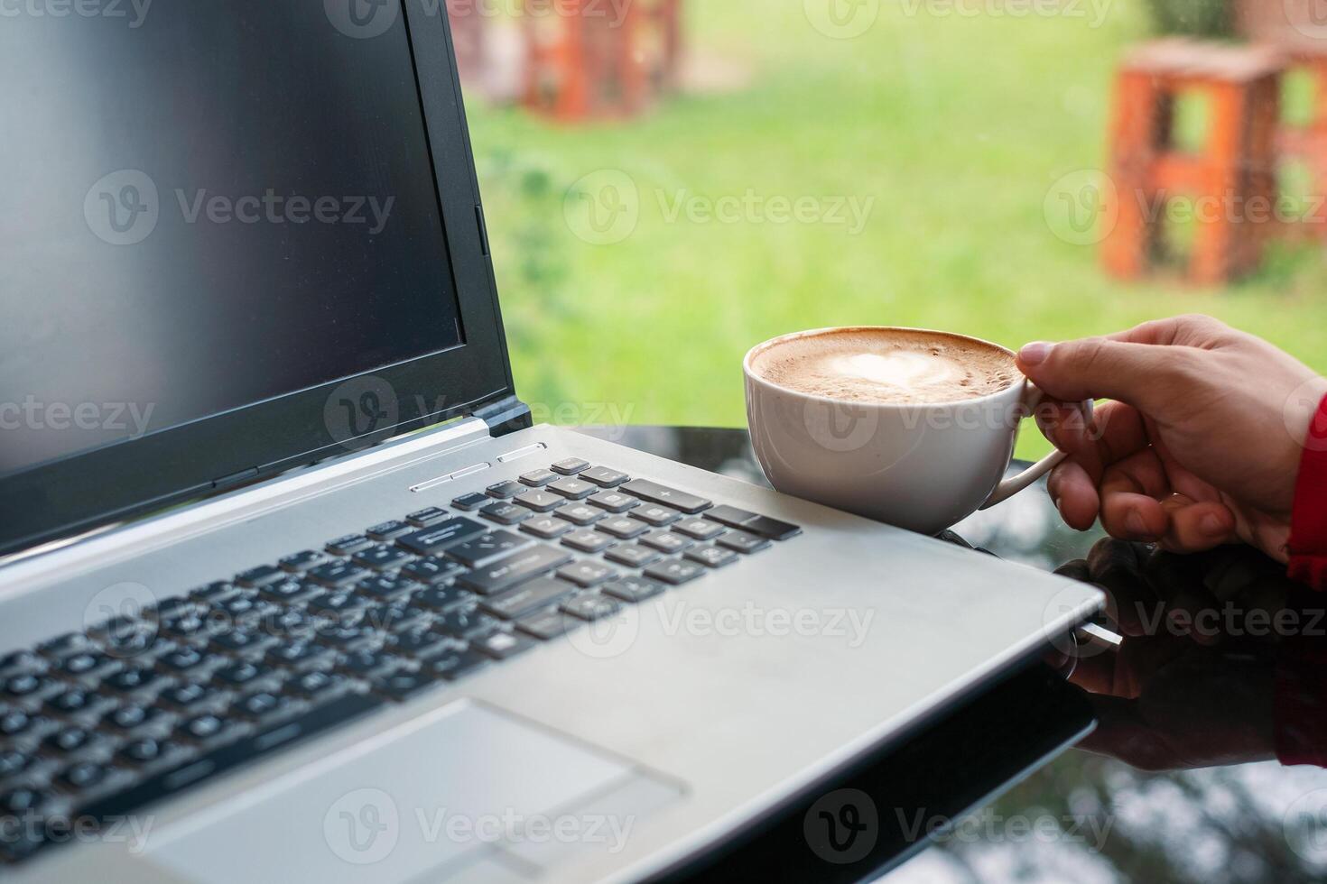 Hand of man holding hot coffee cup with modern laptop in cafe photo