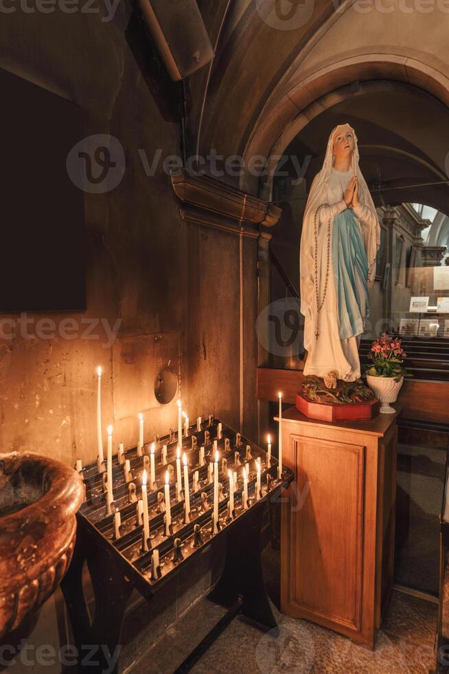 estatua madre Virgen María Orando y luz de una vela altar en cristiano chruch foto