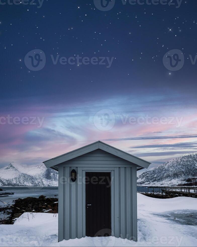 Wooden warehouse and colorful sky with stars on coastline in winter at Senja island photo