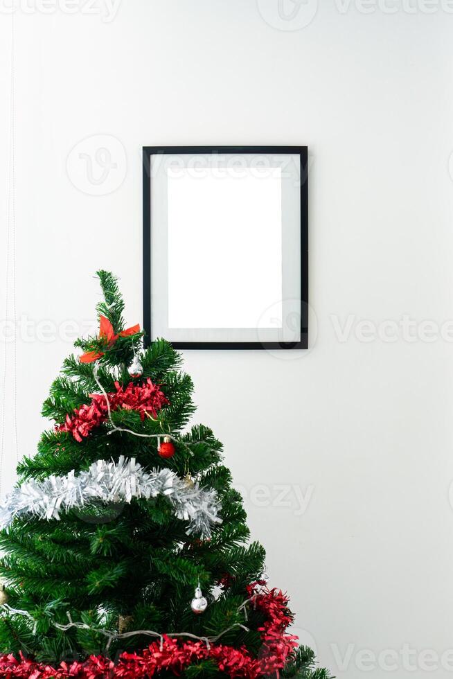 Black picture frame with christmas tree with ball on white wall photo