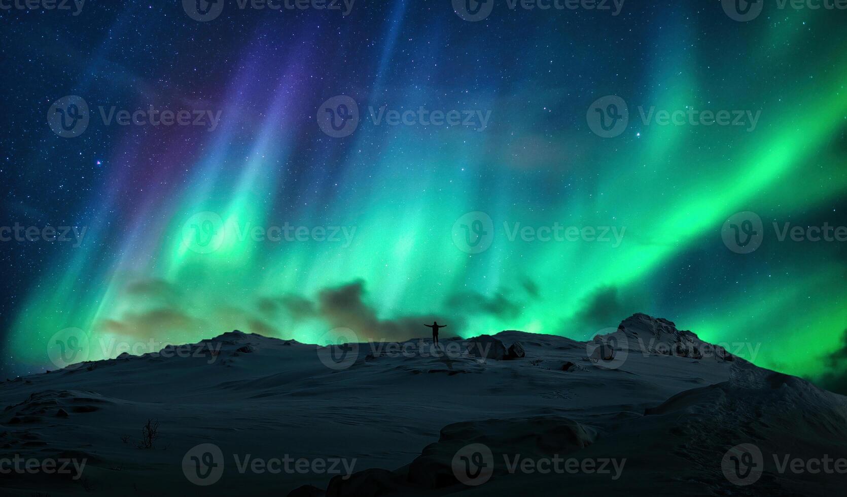 Aurora borealis over silhouette cheerful man on top of mountain in arctic circle at Norway photo