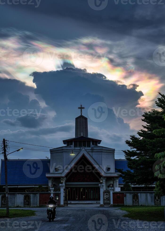 Mysterious cloud iridescence phenomenon glowing over christian church in the evening photo