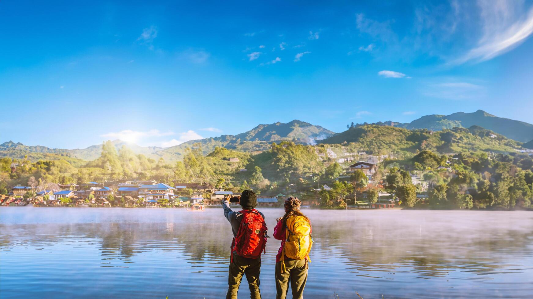 una pareja asiática que está de pie y observa la niebla que se eleva en el lago por la mañana. prohibición de viajes rak thai village, mae hong son en tailandia. toma una foto del lago