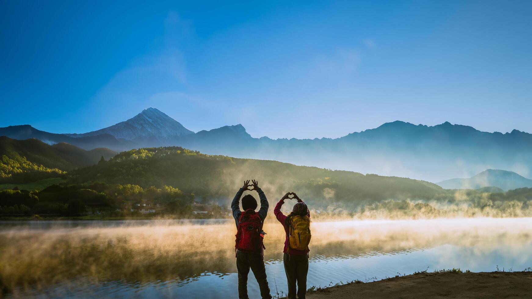 Asian woman and Asian man which backpacking standing near the lake, she was smiling, happy and enjoying the natural beauty of the mist. photo