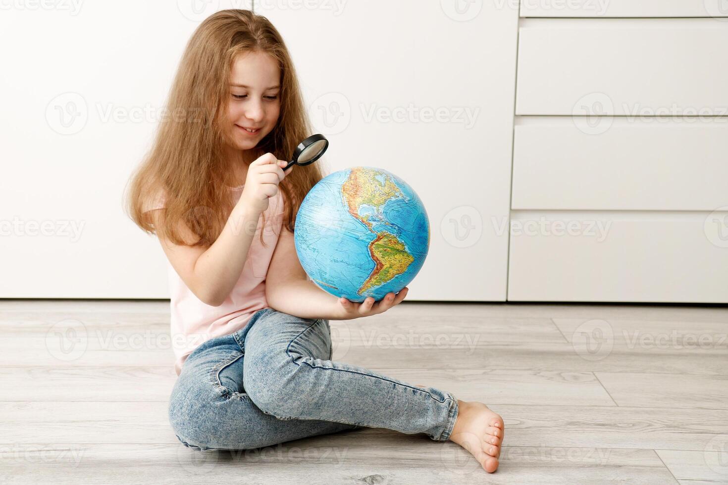 linda sonriente niña mirando a un físico globo mediante un aumentador vaso foto