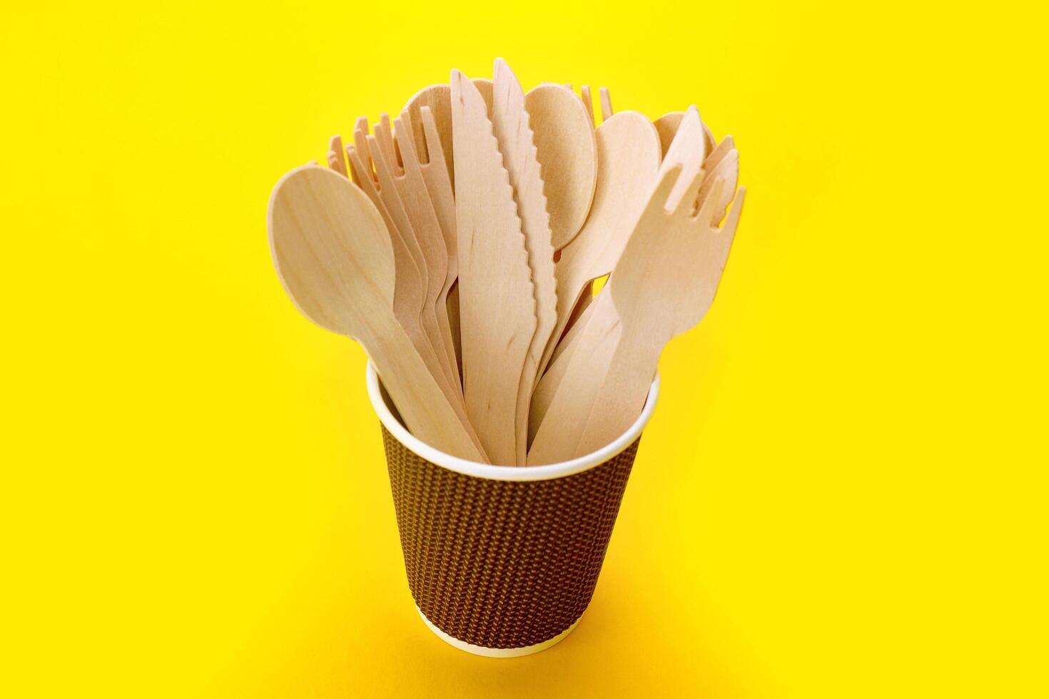 disposable bamboo cutlery in a paper cup on a yellow background, top view photo