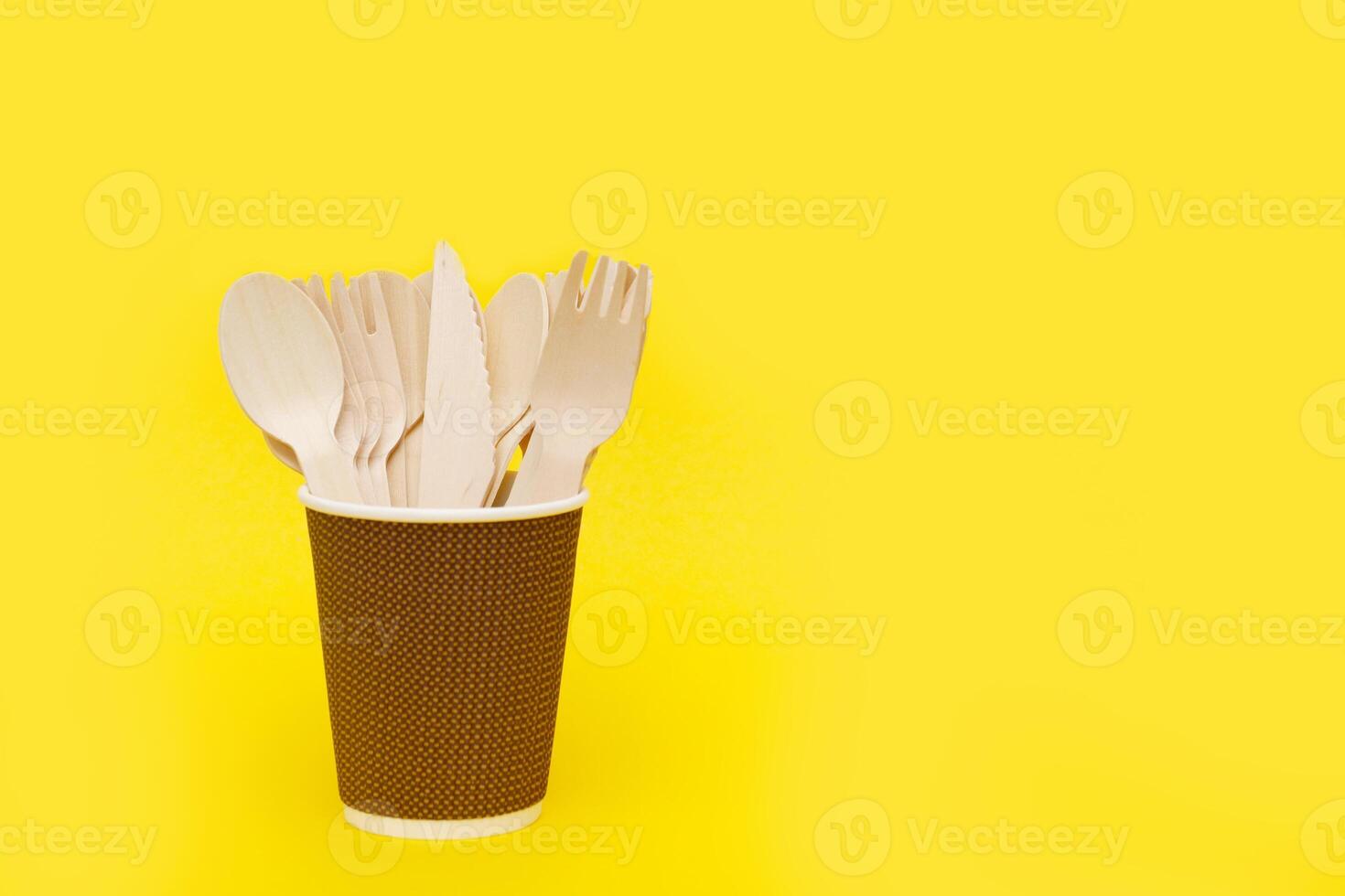 disposable bamboo cutlery in a paper cup on a yellow background with copy space. photo