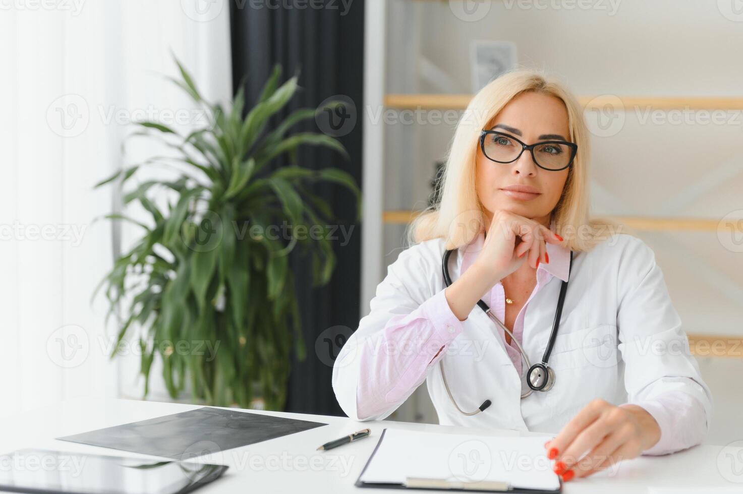 Portrait shot of middle aged female doctor sitting at desk and working in doctor office photo