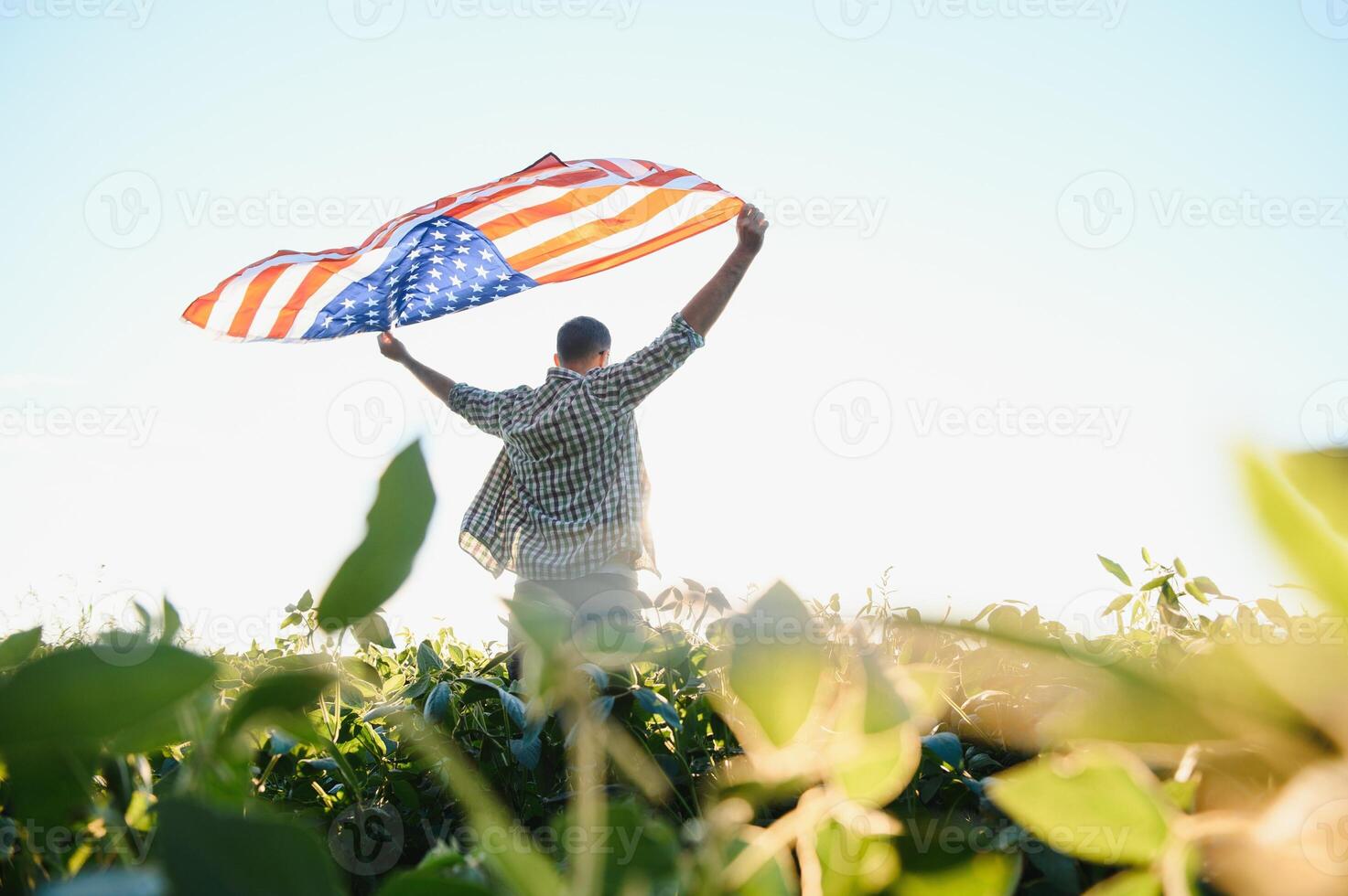 A young farmer stands with a USA flag in a soybean field. The concept of the US agricultural industry. photo