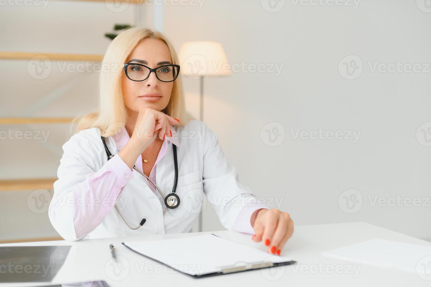 Portrait of middle age female doctor is wearing a white doctor's coat with a stethoscope around her neck. Smiling physician standing at private clinic photo