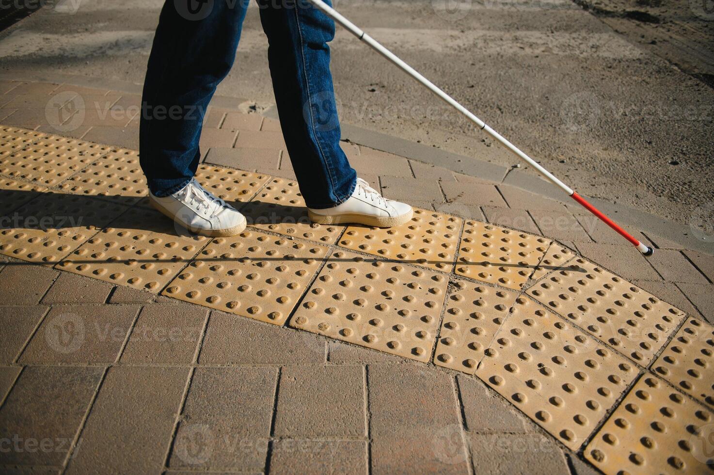 young blind man with white cane walking across the street in city photo
