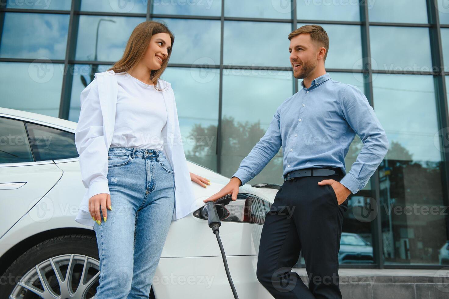 contento joven adulto hombre y sonriente mujer cargando eléctrico coche. foto