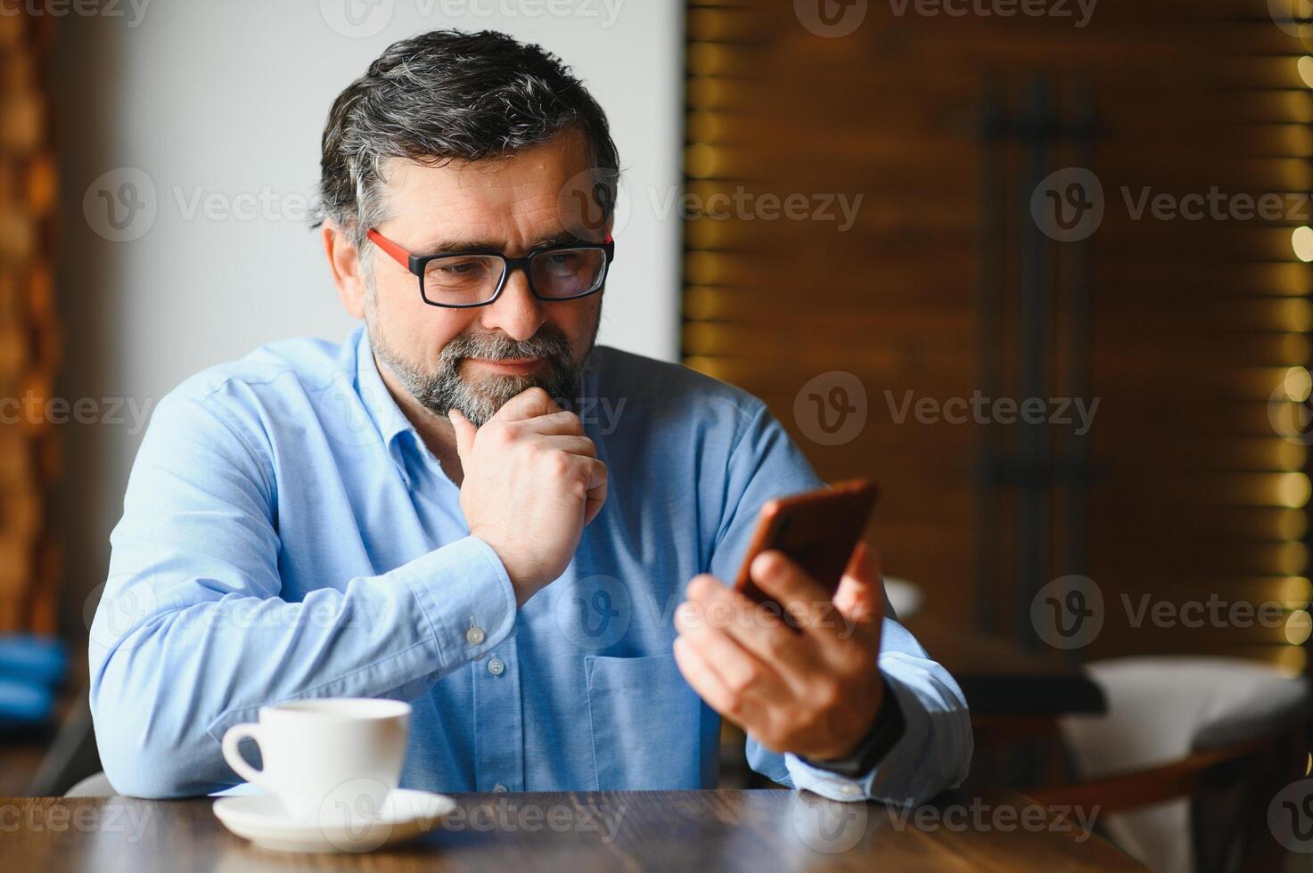 contento empresario sentado en restaurante y esperando para almuerzo. él es utilizando inteligente teléfono y hablando con alguien. negocio personas mayores estilo de vida concepto. foto
