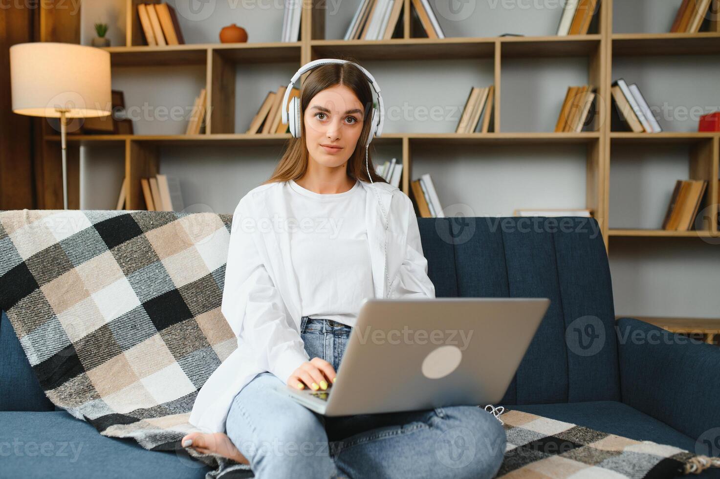 Smiling attractive young woman sitting on sofa using laptop communicating working online at home, happy teen girl typing on computer, enjoying writing blog or chatting with friends in social network photo