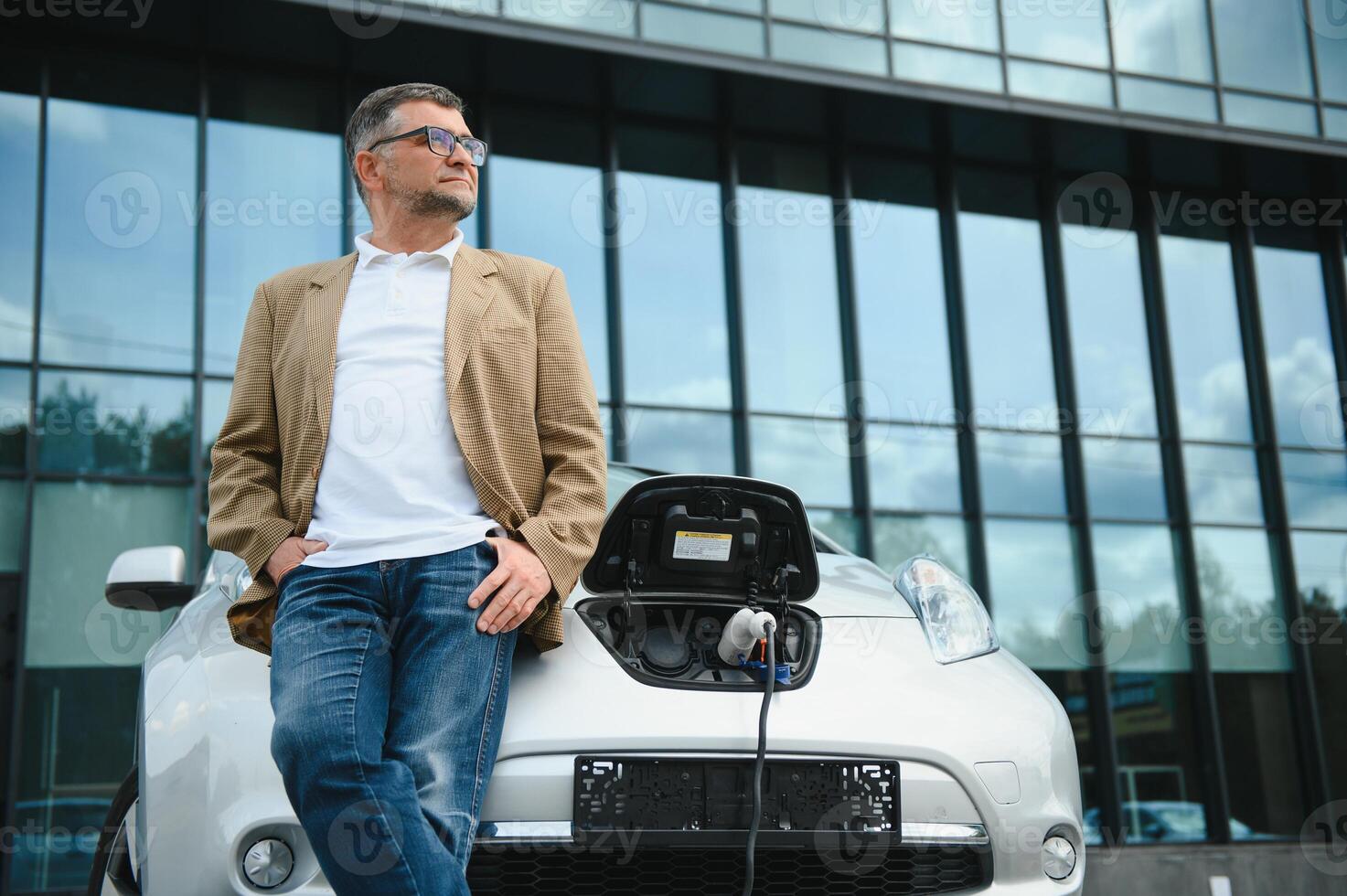 Casual man near electric car waiting for the finish of the battery charging process. photo