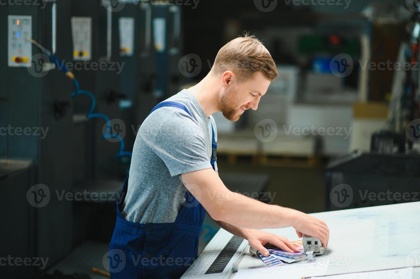Portrait of production line worker controlling manufacturing process of modern packaging industrial machine in printing factory photo