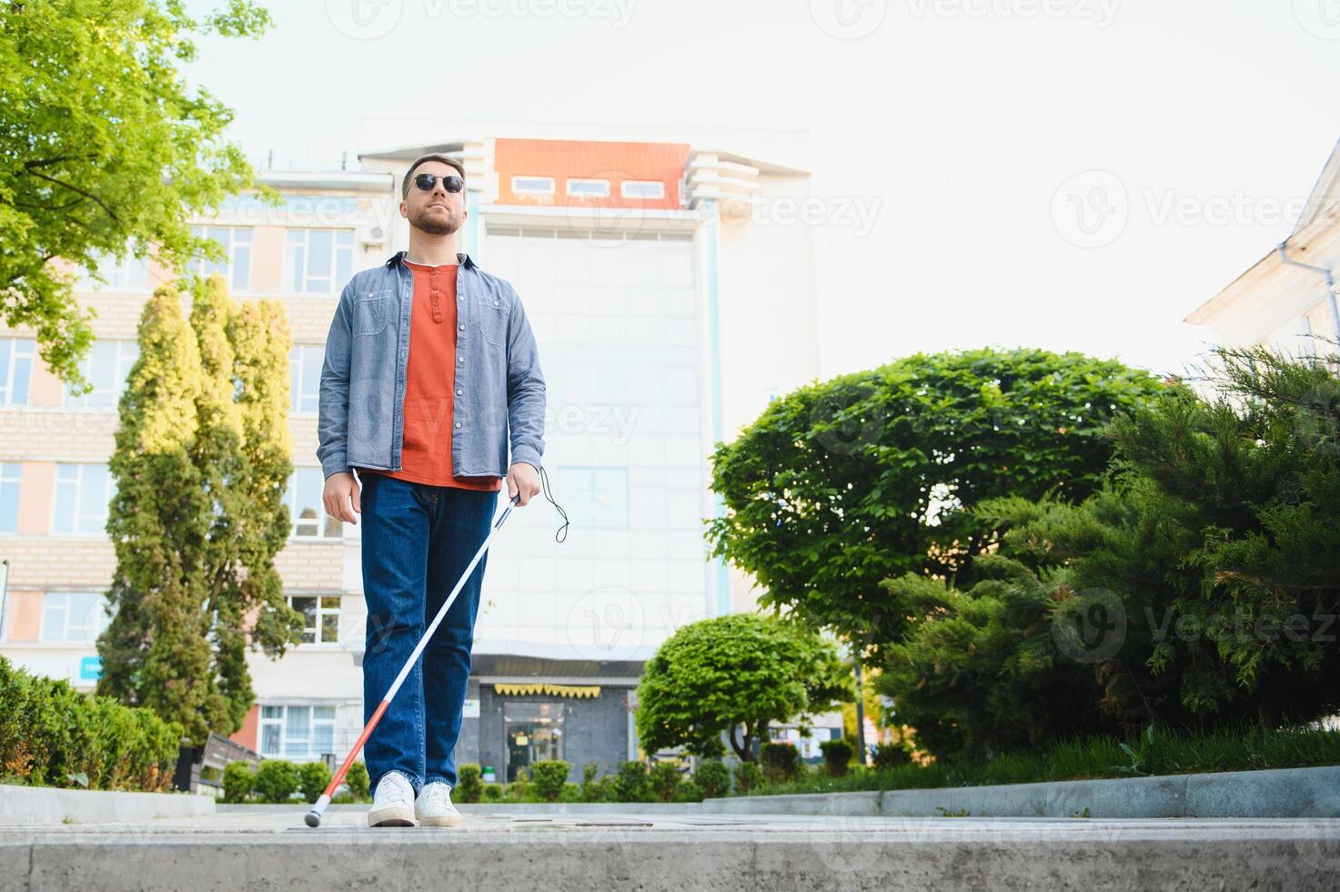 young blind man with white cane walking across the street in city photo