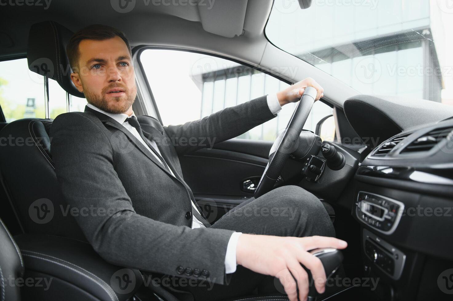 Man of style and status. Handsome young man in full suit smiling while driving a car photo