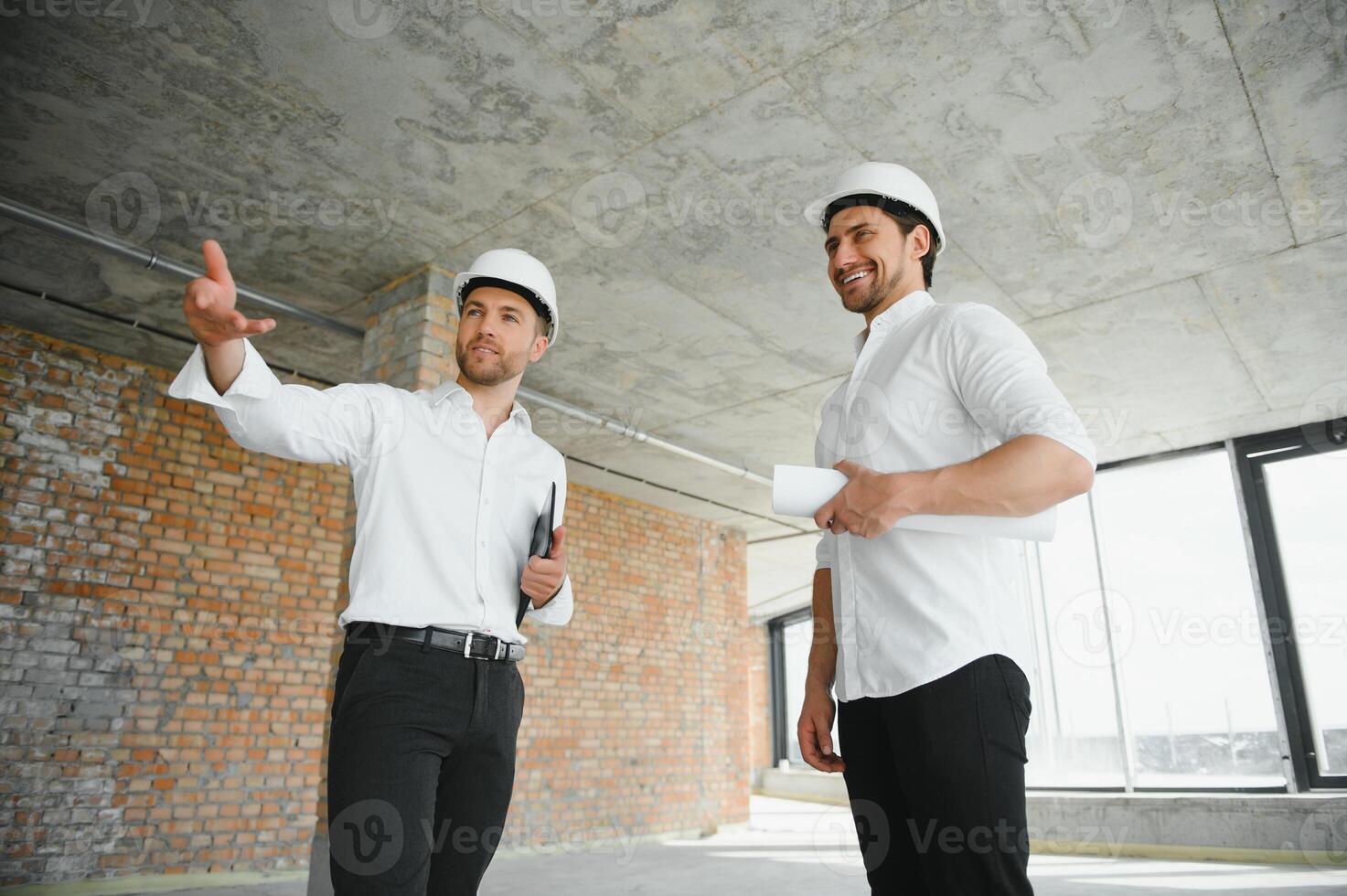 A front view of two smart architects with white helmets reviewing blueprints at a construction site on a bright sunny day photo