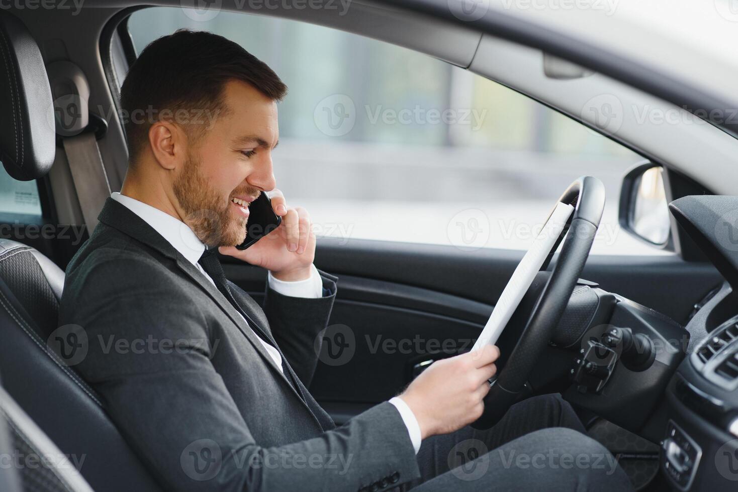 Always in a hurry. Handsome young man in full suit smiling while driving a car. photo