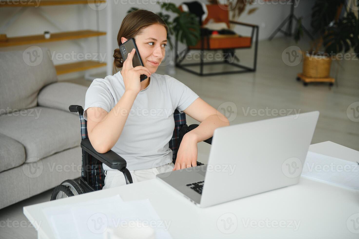 Female freelance programmer sitting in wheelchair and using computers while coding web game at home. photo