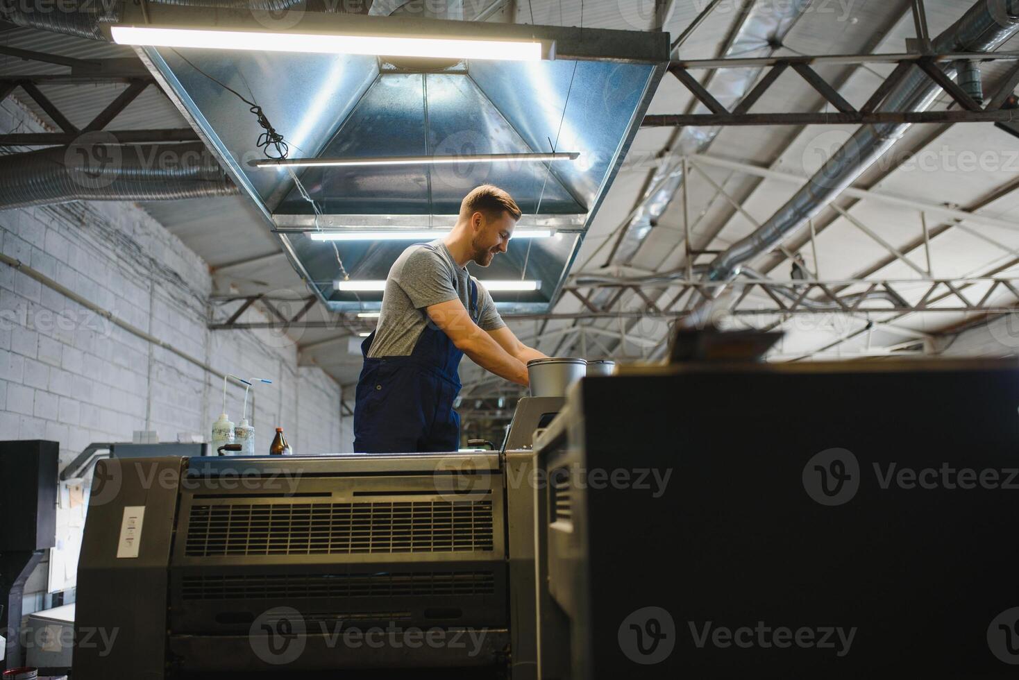 Portrait of production line worker controlling manufacturing process of modern packaging industrial machine in printing factory photo