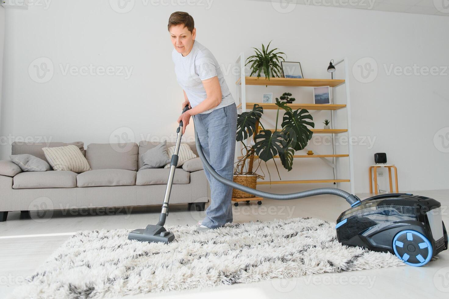 Portrait of senior woman with vacuum cleaner indoors at home, hoovering photo