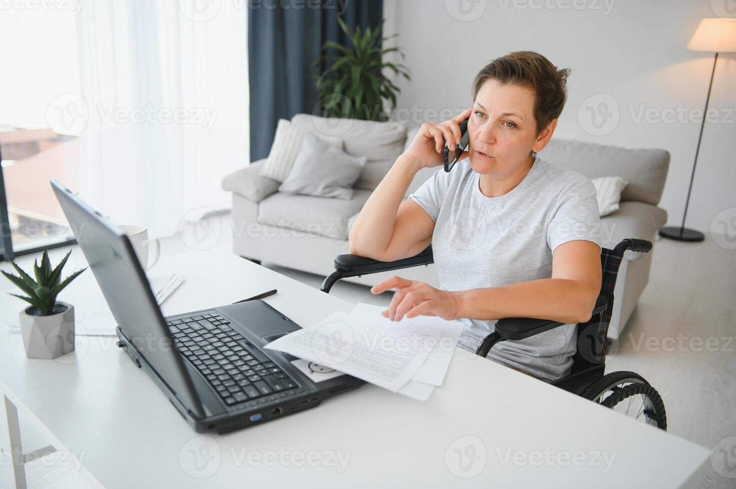 Freelancer in wheelchair using laptop near notebook and papers on table photo