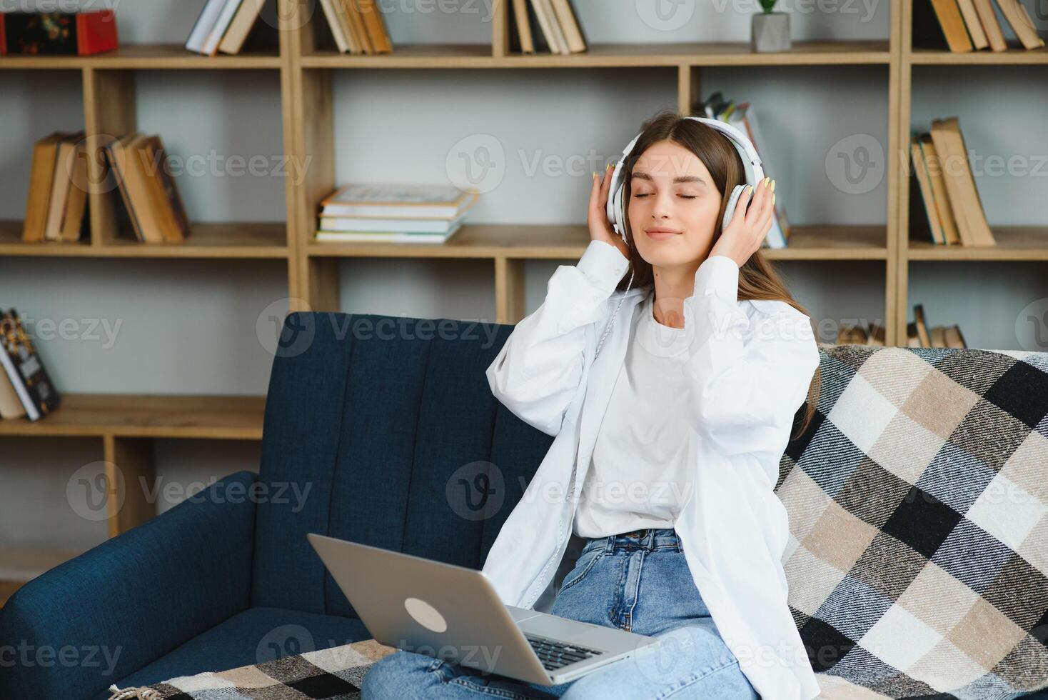 Beautiful young caucasian woman in casual clothing enjoying music and smiling while resting at home. Young woman with headphones using laptop at home photo