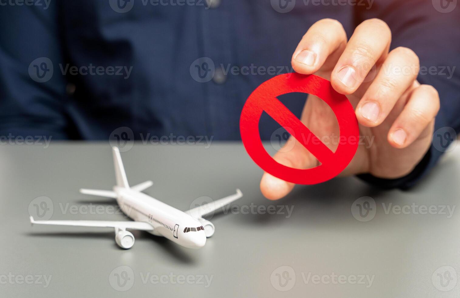 A man holds a prohibitory sign near an airplane. Sanctions. Refusal of aircraft insurance, breaking leasing agreements. Closing air routes. Flight cancellation. Failure safety tests. Restrictions photo