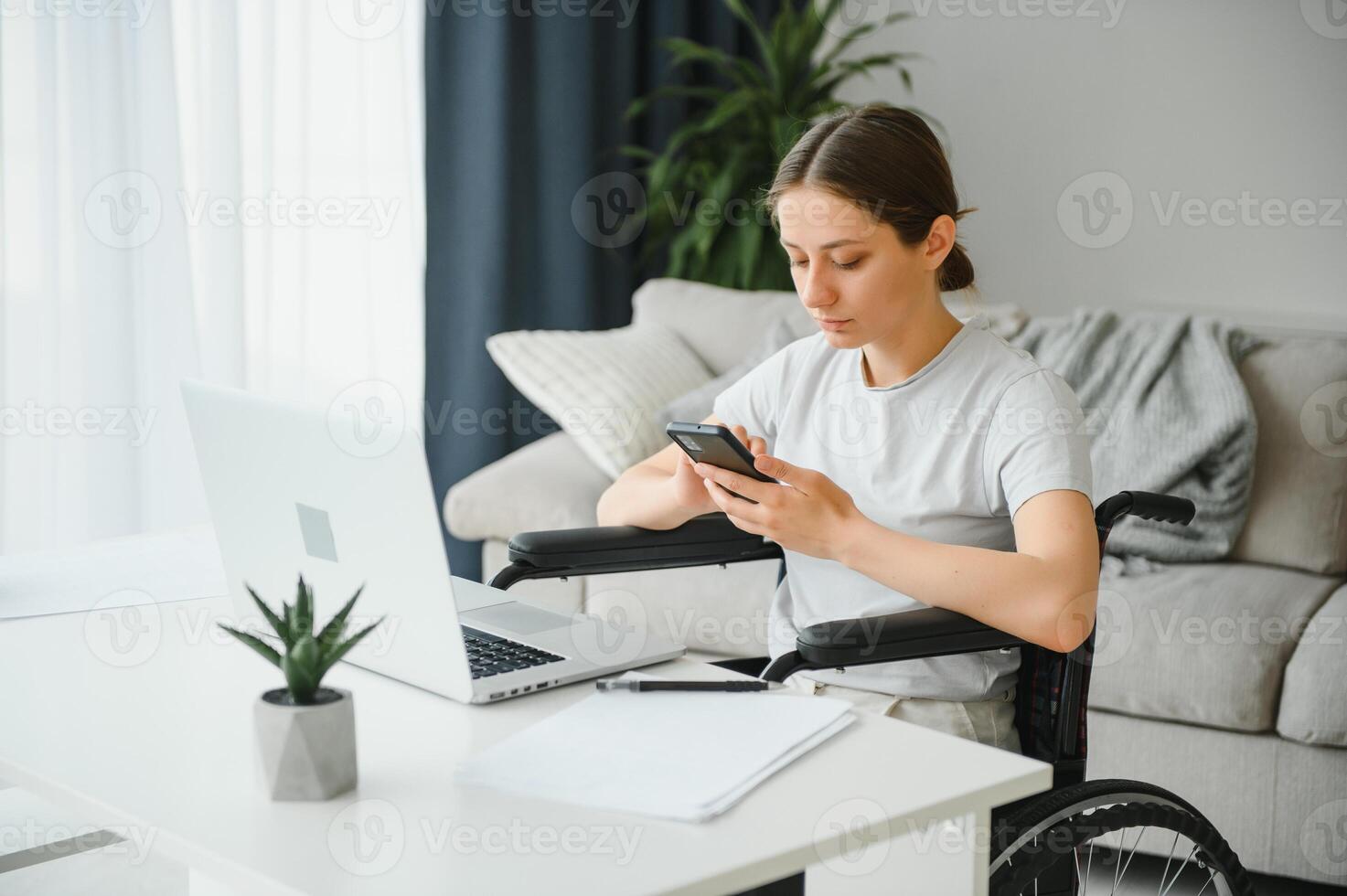 Female freelance programmer sitting in wheelchair and using computers while coding web game at home. photo