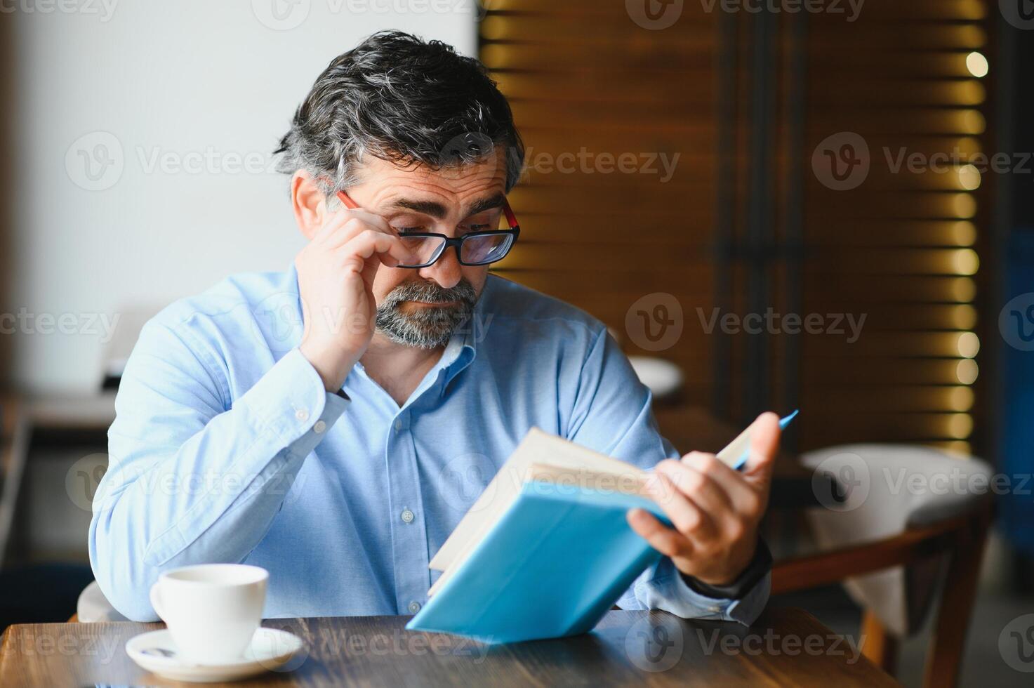 Senior old man reading a book in a coffee shop, enjoying his literary hobby photo