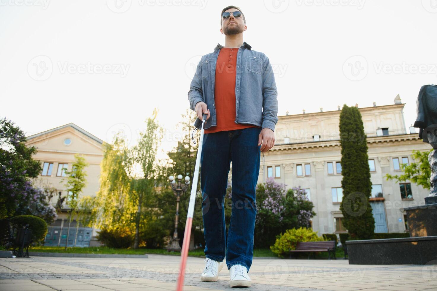 Young handsome blinded man walking with stick in town photo