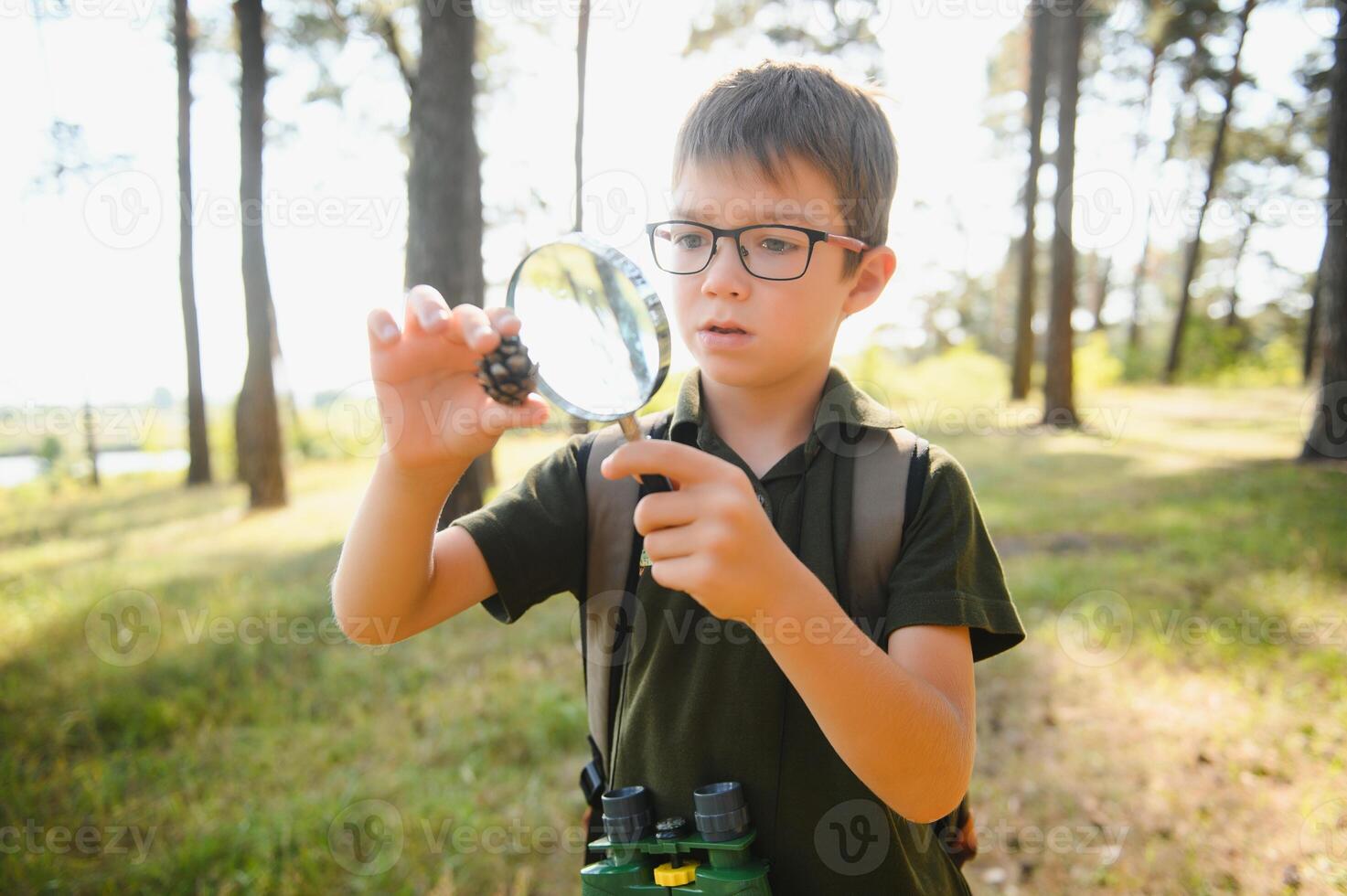 schoolboy is exploring nature with magnifying glass. Summer vacation for inquisitive kids in forest. Hiking. Boy-scout. photo